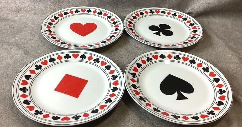 Four white dessert plates with black and red playing card suit centers, view 2