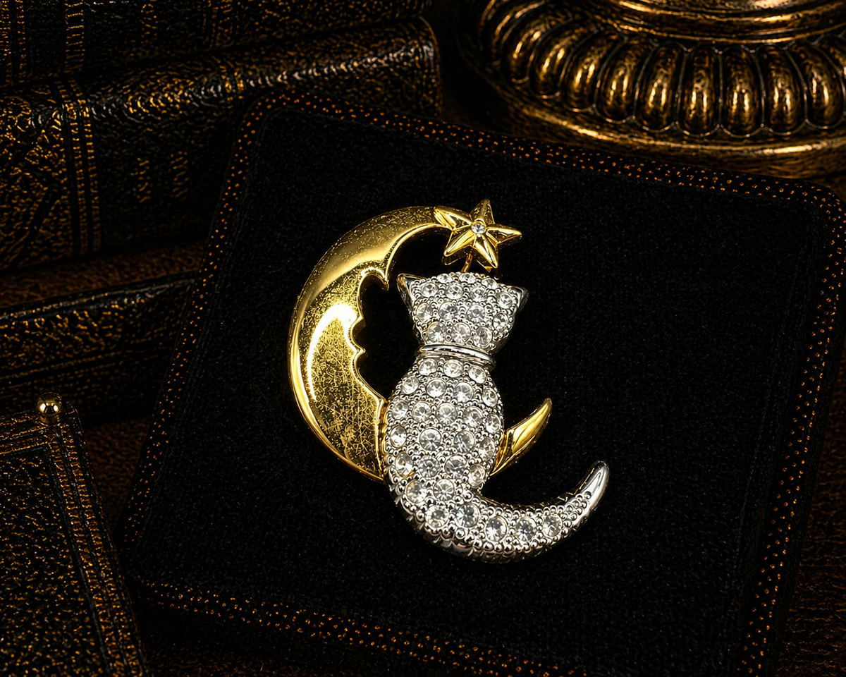 Two-tone brooch of a clear crystal cat on a gold-tone crescent moon with star