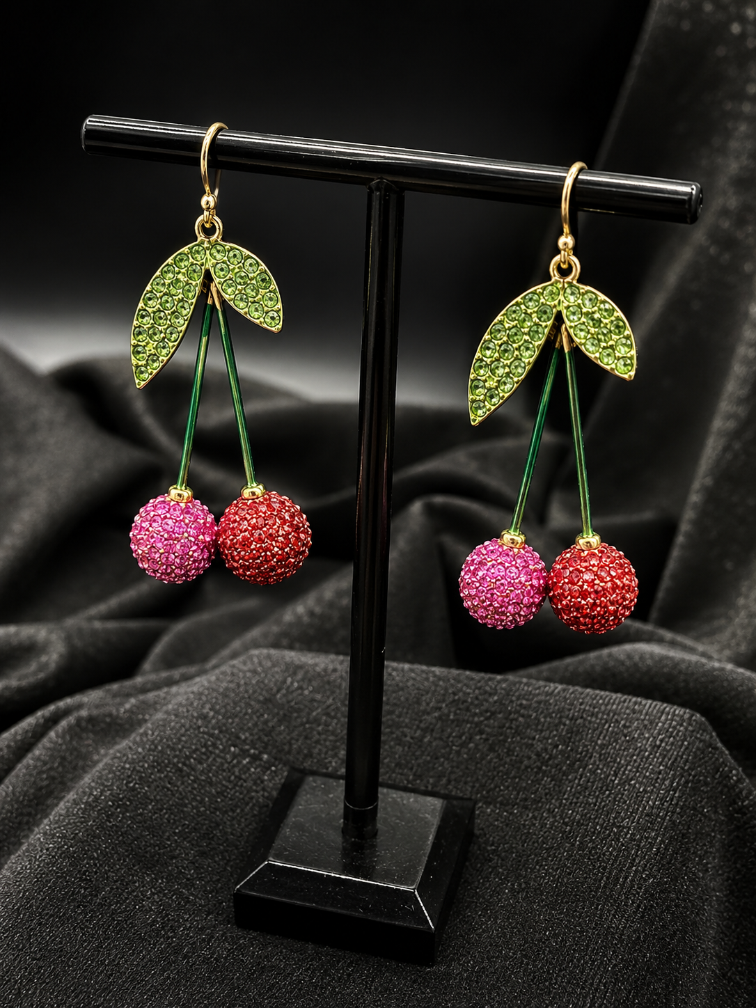 Pink crystal cherry dangle earrings with green stems and leaves on gold-tone hooks
