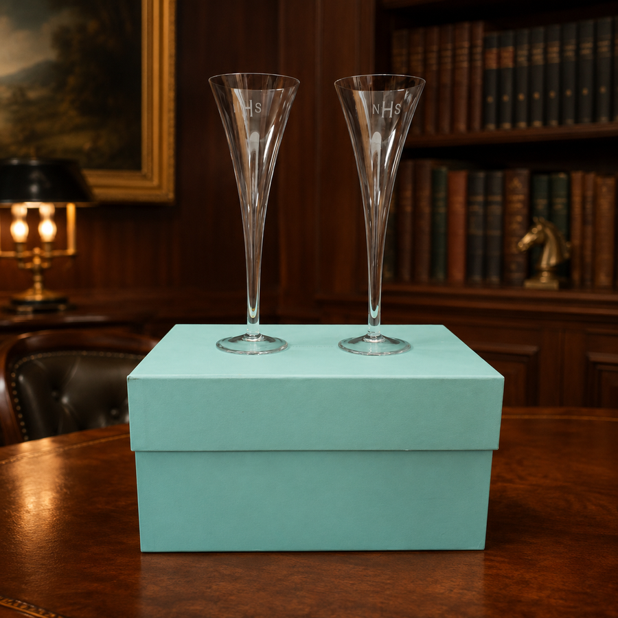 Two tall clear champagne flutes etched with the initials NHS beside a blue box